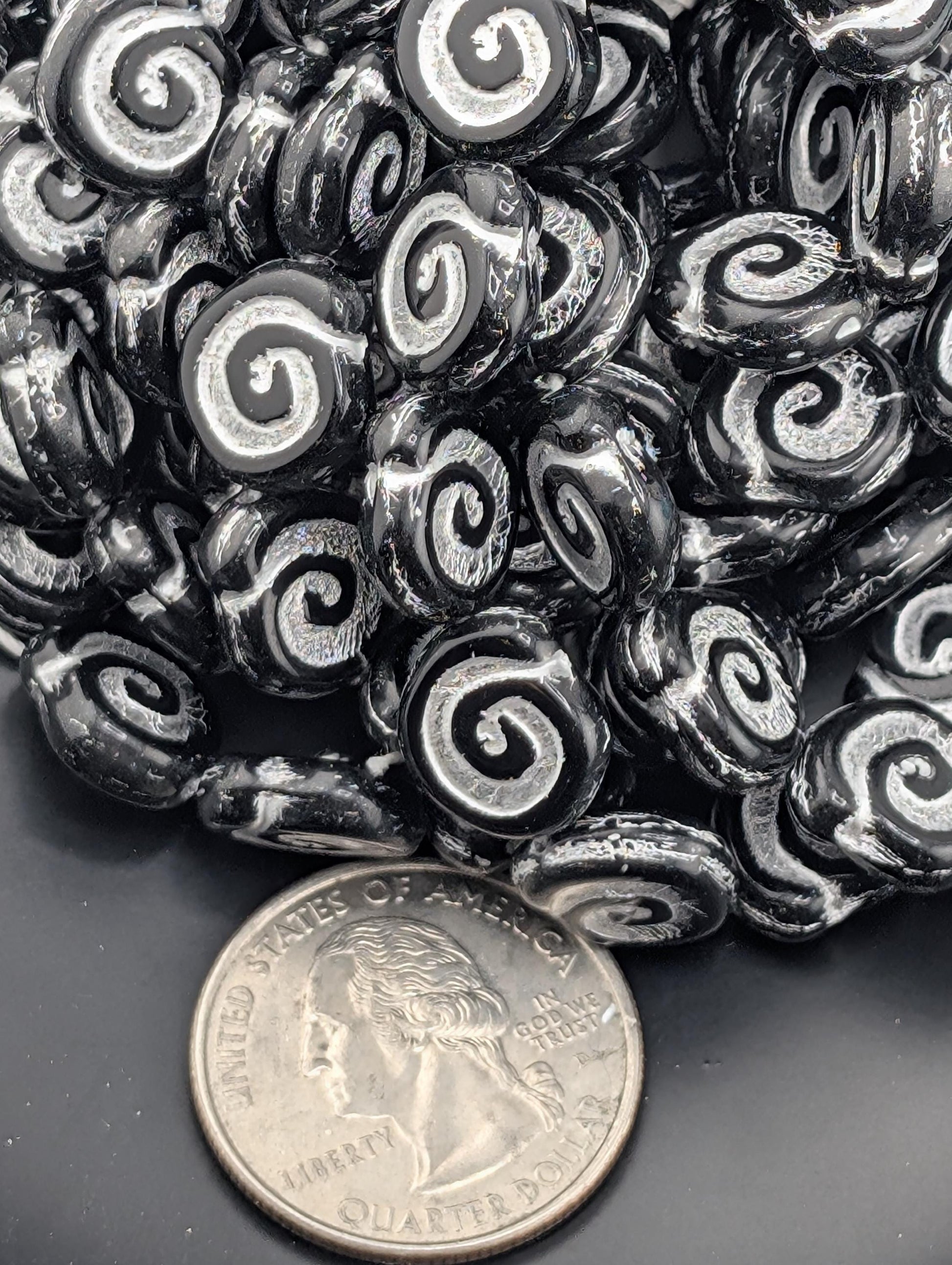 a pile of black and white spiral beads next to a United States quarter coin.