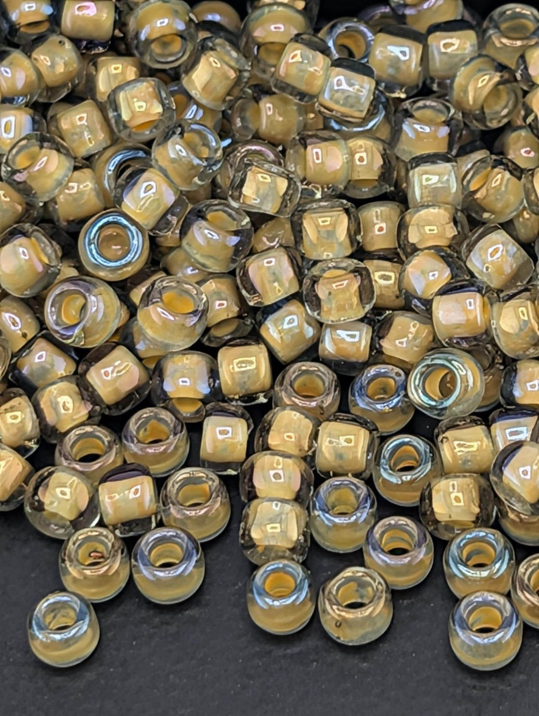 a large pile of small, clear beads in various shades of yellow and brown, scattered on a dark surface.