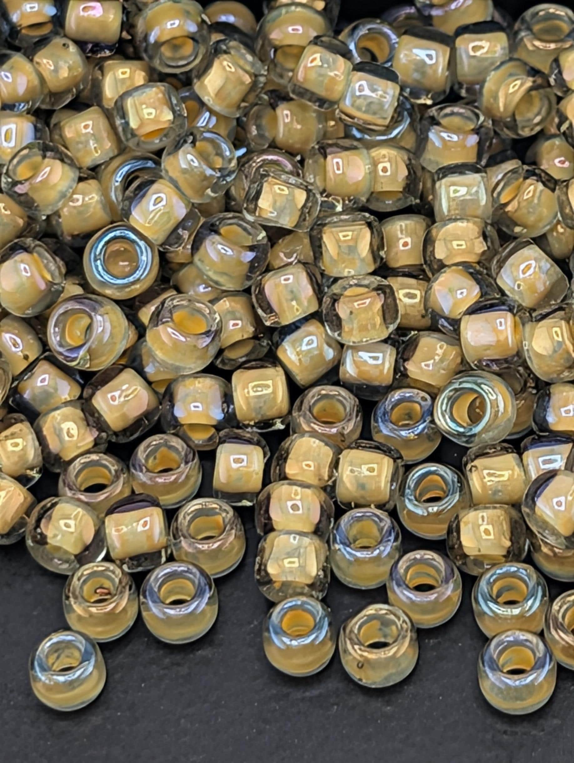 a large pile of small, clear beads in various shades of yellow and brown, scattered on a dark surface.