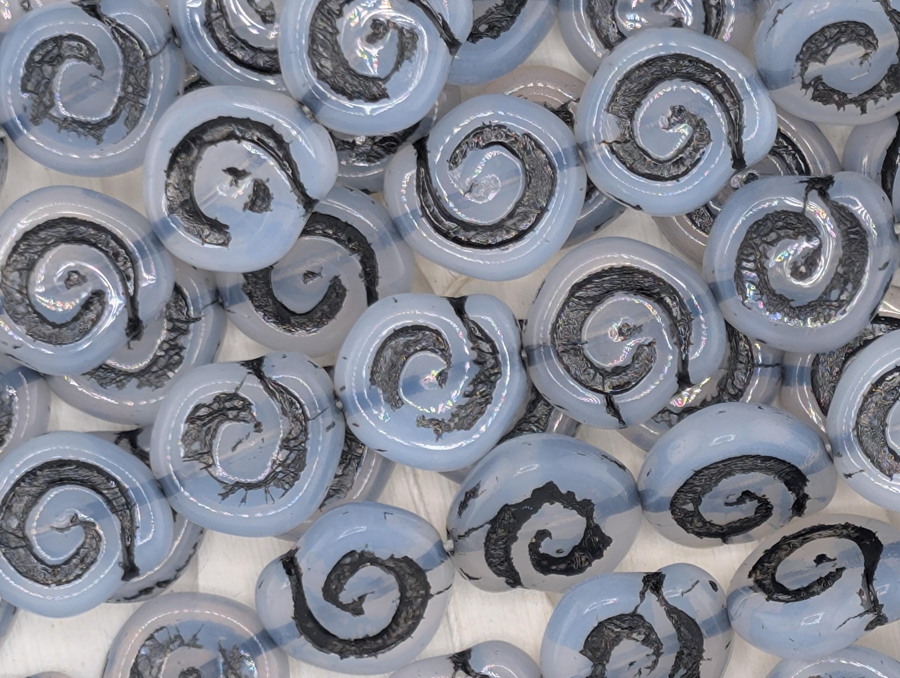 numerous spiral-shaped objects, some of which appear to be made of glass or a similar material. The objects have a black and white color scheme, with some of them having a metallic or black-and-white pattern. The objects are arranged in a scattered manner, creating a visually interesting and dynamic composition.