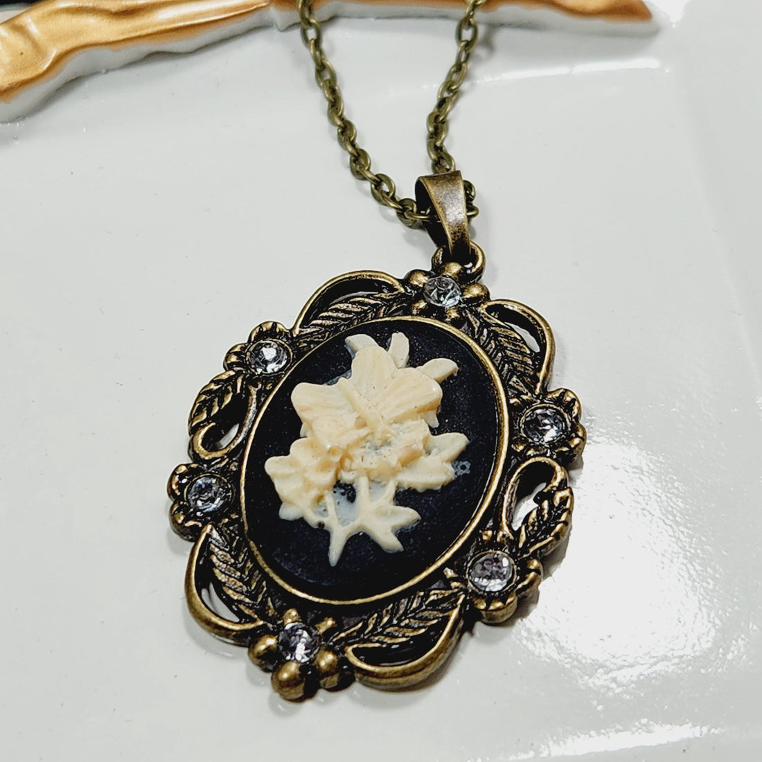 A decorative pendant with a floral design and a chain is shown in the image.