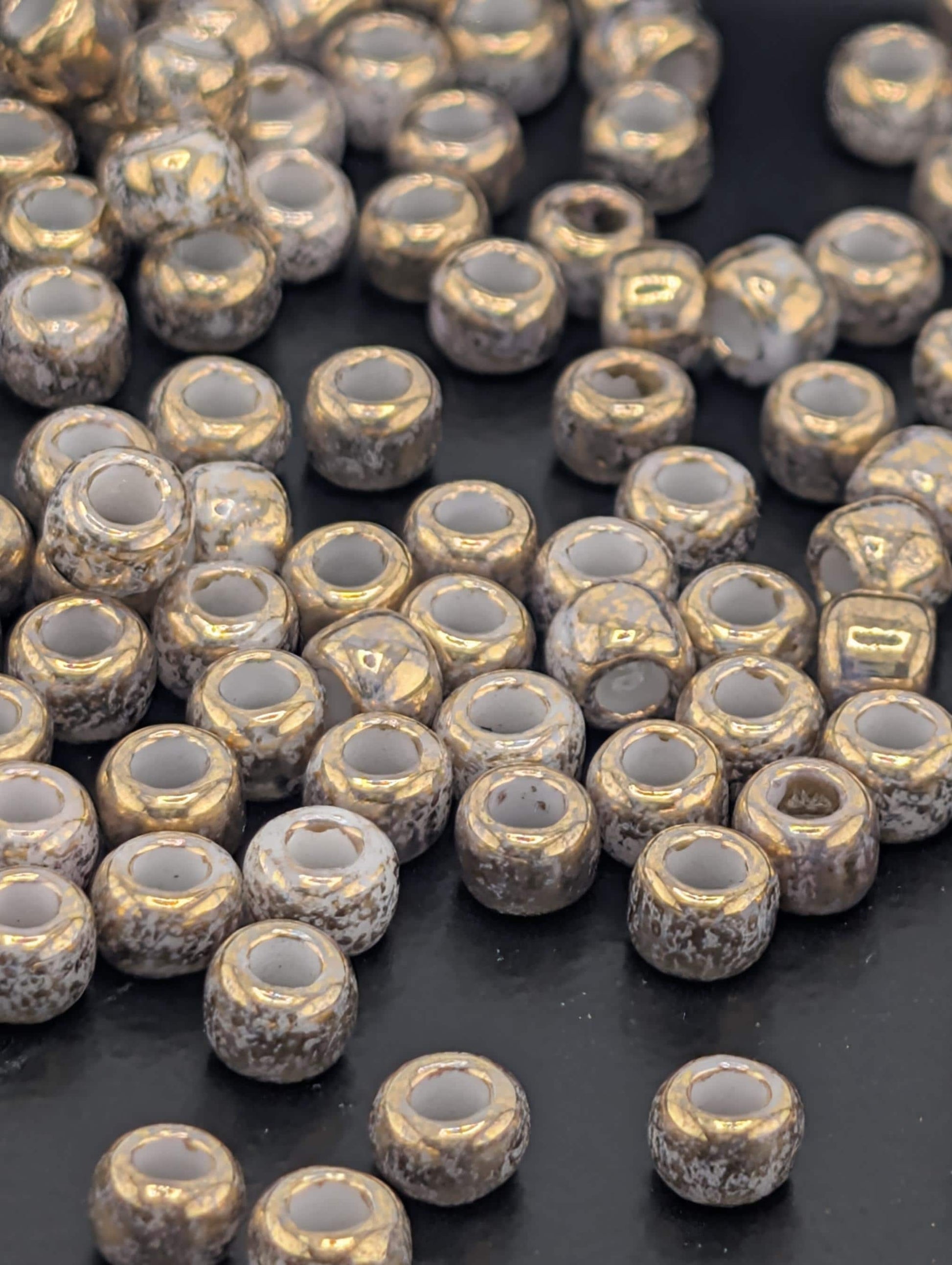 a collection of small, round beads scattered on a dark surface. The beads have a shiny, metallic appearance and are arranged in a somewhat haphazard manner, creating a sense of randomness and depth.