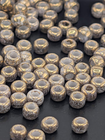 a collection of small, round beads scattered on a dark surface. The beads have a shiny, metallic appearance and are arranged in a somewhat haphazard manner, creating a sense of randomness and depth.