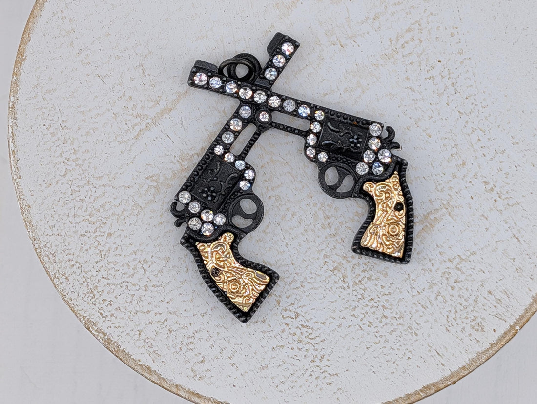 A decorative pendant featuring two ornate gun-like figures with intricate designs and sparkling rhinestones.