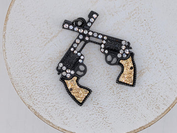A decorative pendant featuring two ornate gun-like figures with intricate designs and sparkling rhinestones.