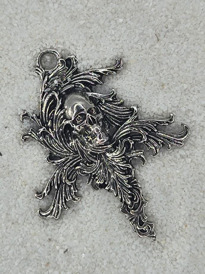 a silver-colored pendant with an intricate design, including a skull and ornate, decorative elements.