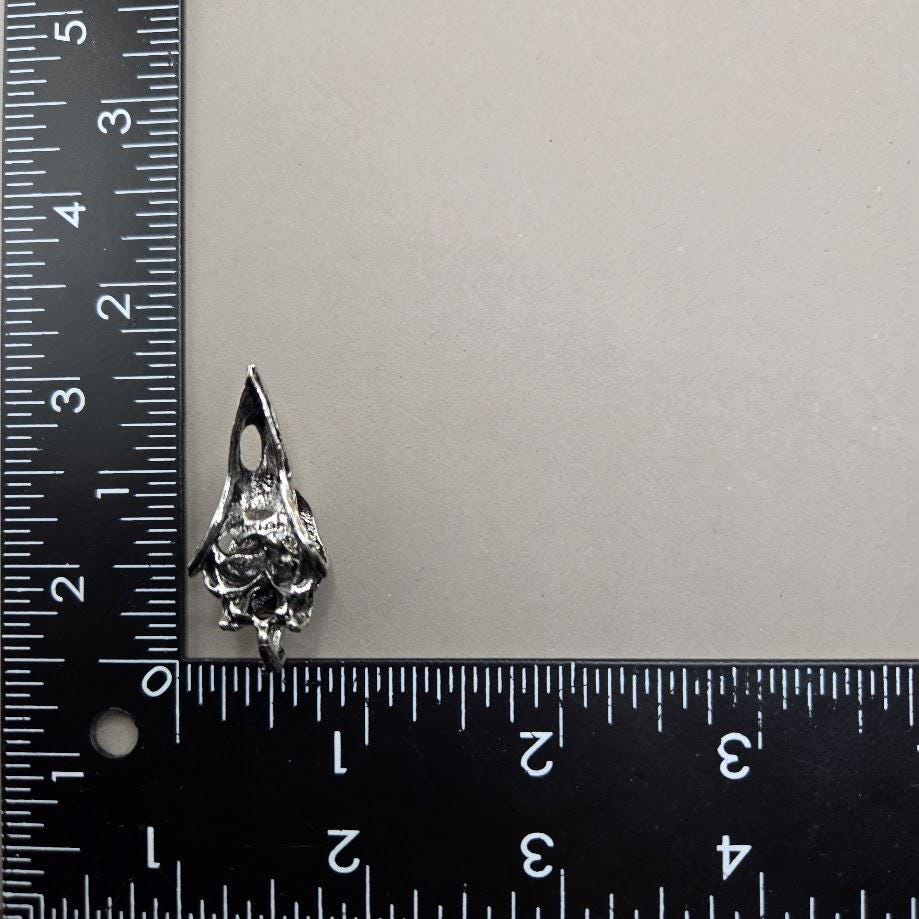 A silver-colored pendant or ornament is placed next to a ruler on a gray surface.