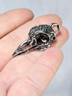 A hand holding a small, intricately designed metal bird skull pendant.