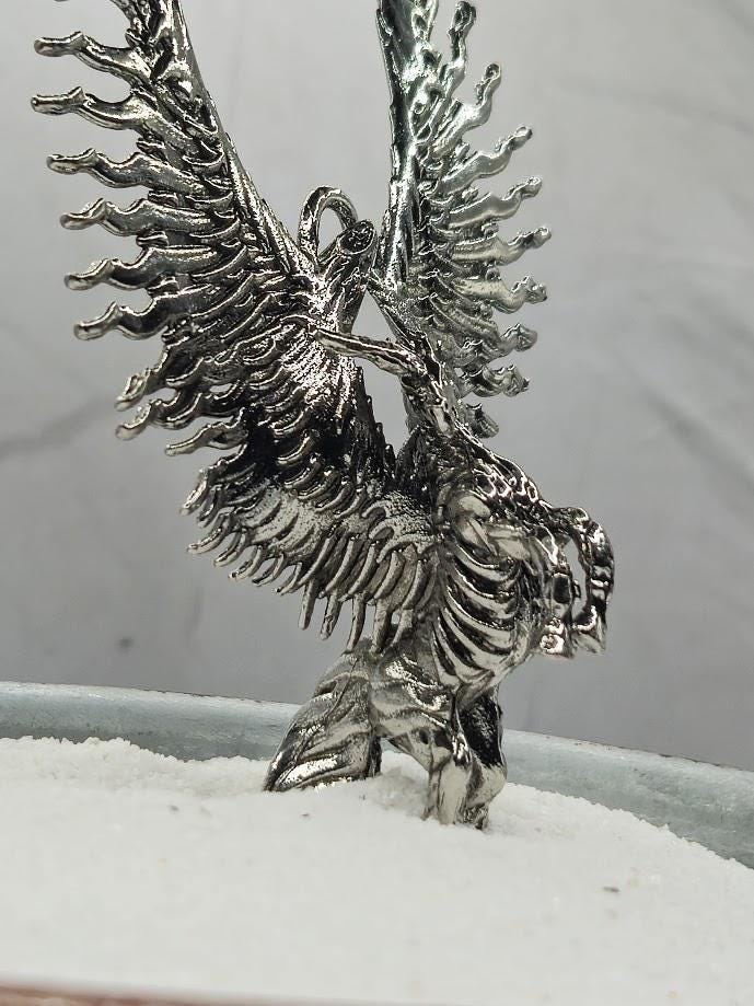 A silver metal sculpture of a winged creature with intricate details and a metallic sheen.