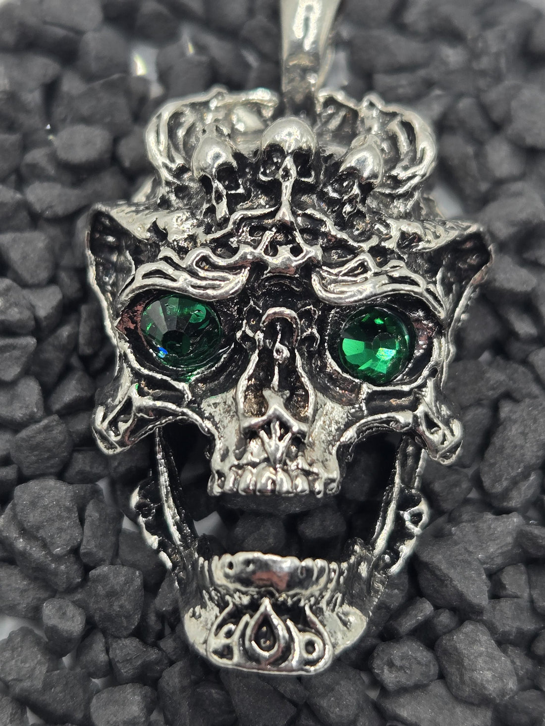 A silver-toned pendant in the shape of a skull with green gemstones on the eyes.