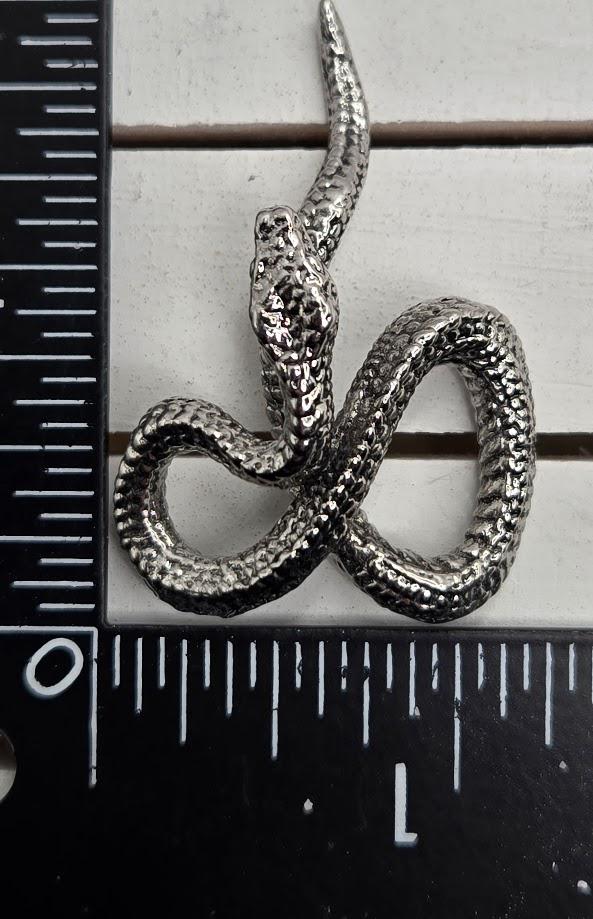 A close-up image of a snake-shaped object, possibly a pendant or sculpture, placed next to a ruler for size comparison.