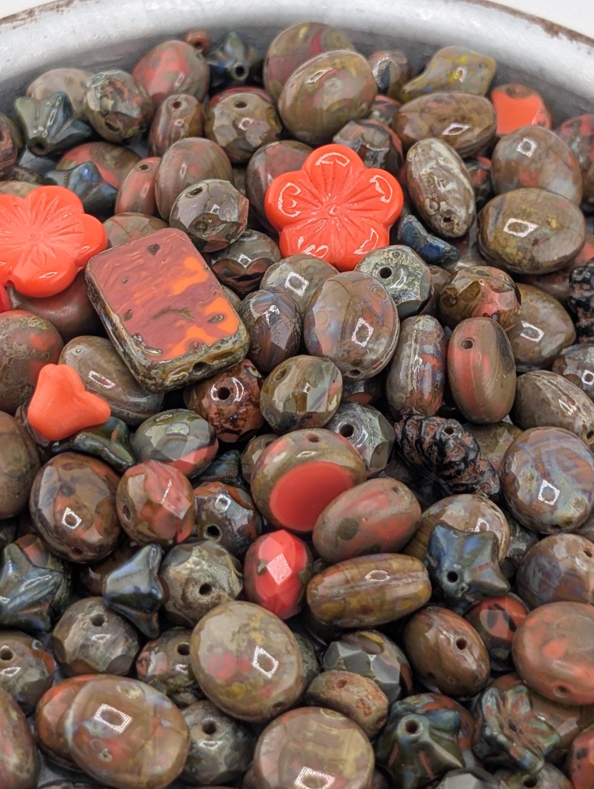 a close-up view of a collection of various colored beads, including red, brown, and black beads, as well as some orange and red beads. The beads are scattered together, creating a visually interesting and diverse assortment.