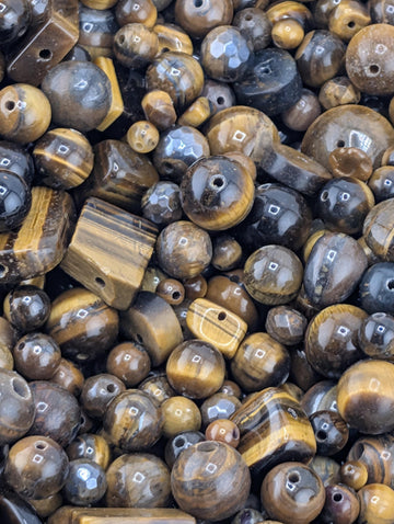 The image is a close-up of various beads and gemstones, including tiger eye beads, arranged in a visually appealing manner.