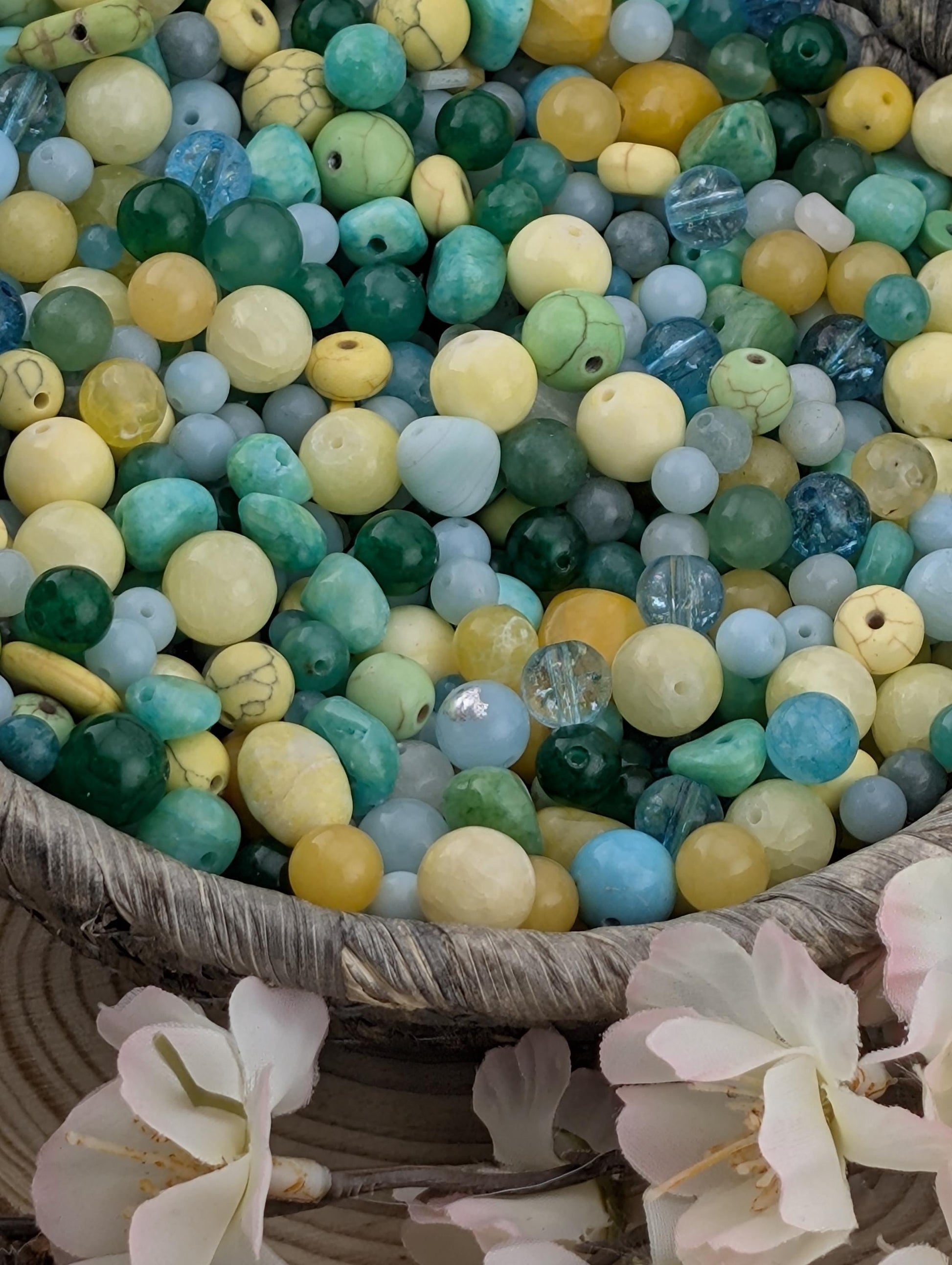A basket filled with a variety of colorful beads, including turquoise, yellow, and white beads, along with some pink flowers.