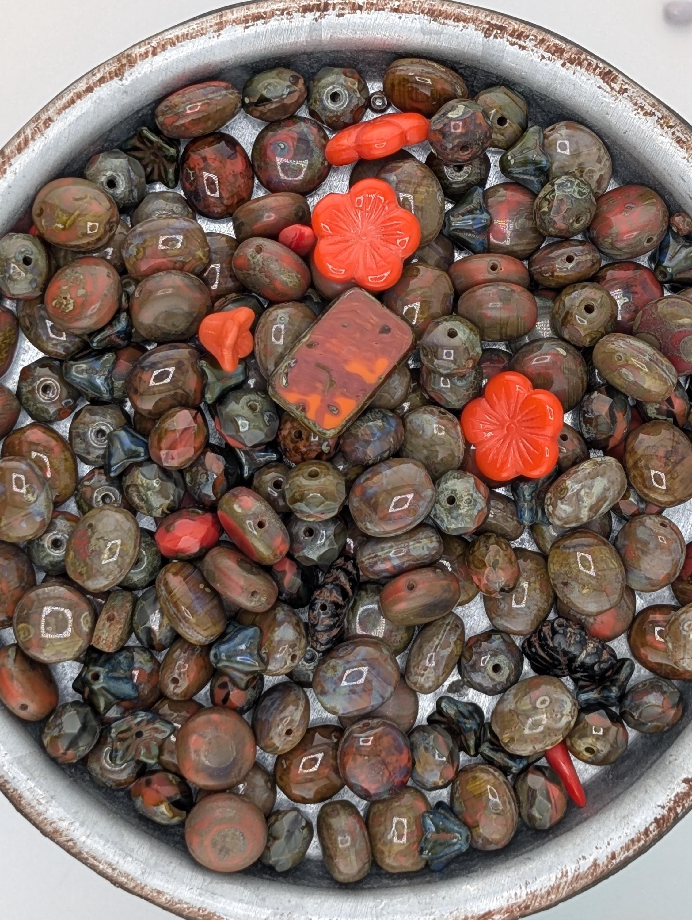 a bowl filled with various colored beads, including red, orange, and brown, as well as some small orange flowers.