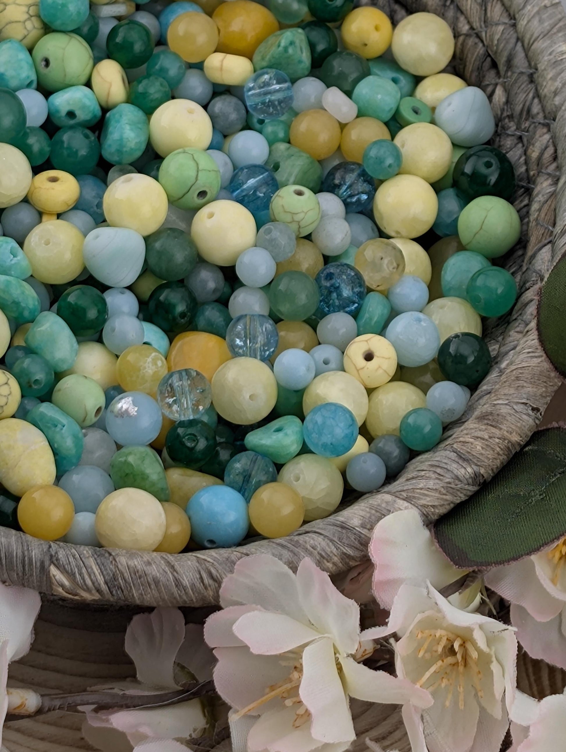A basket filled with a variety of colorful beads, including blue, green, yellow, and white beads, along with some flowers.