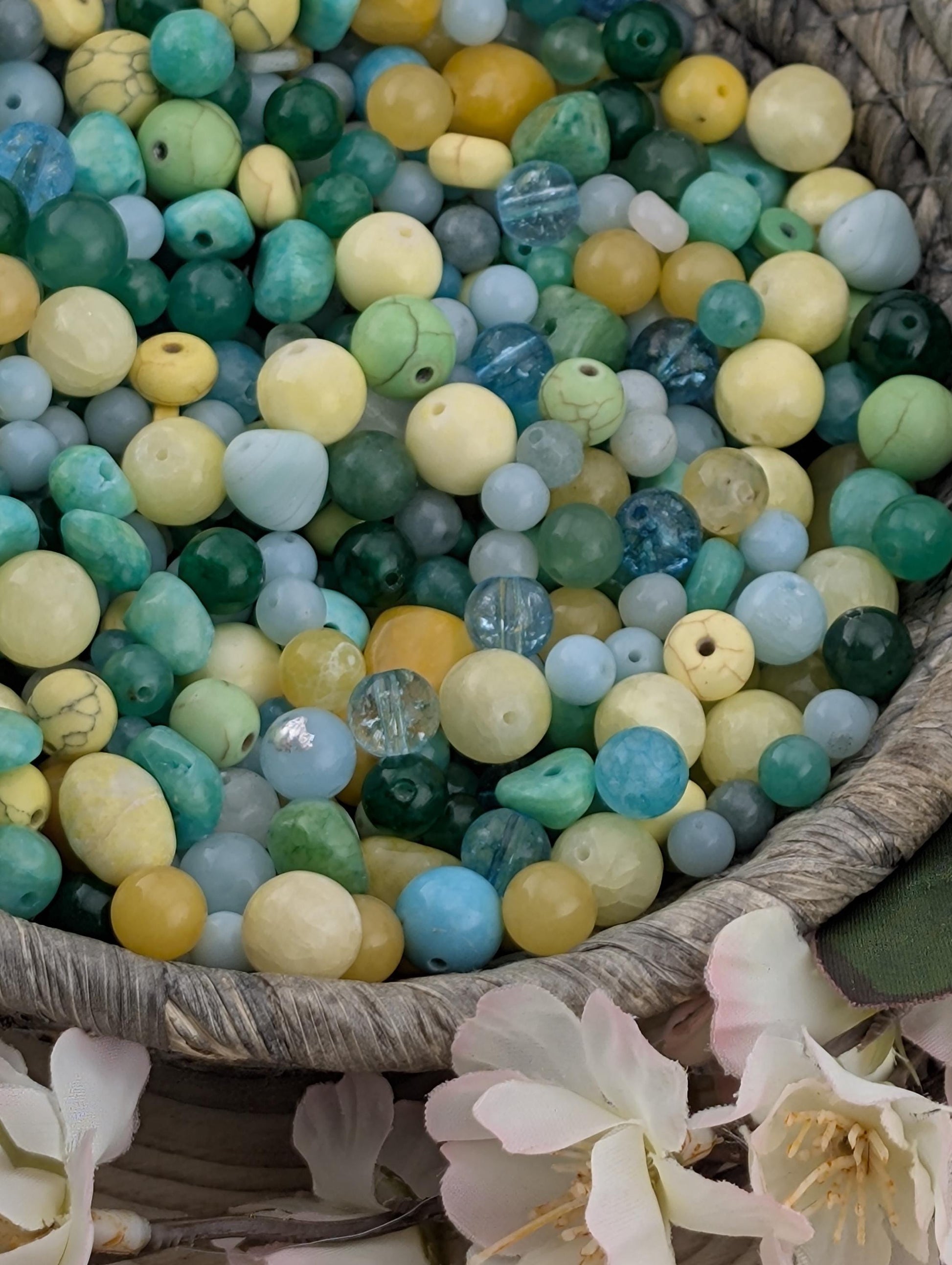 a basket filled with various colored beads, including blue, green, yellow, and white beads, as well as some flowers.