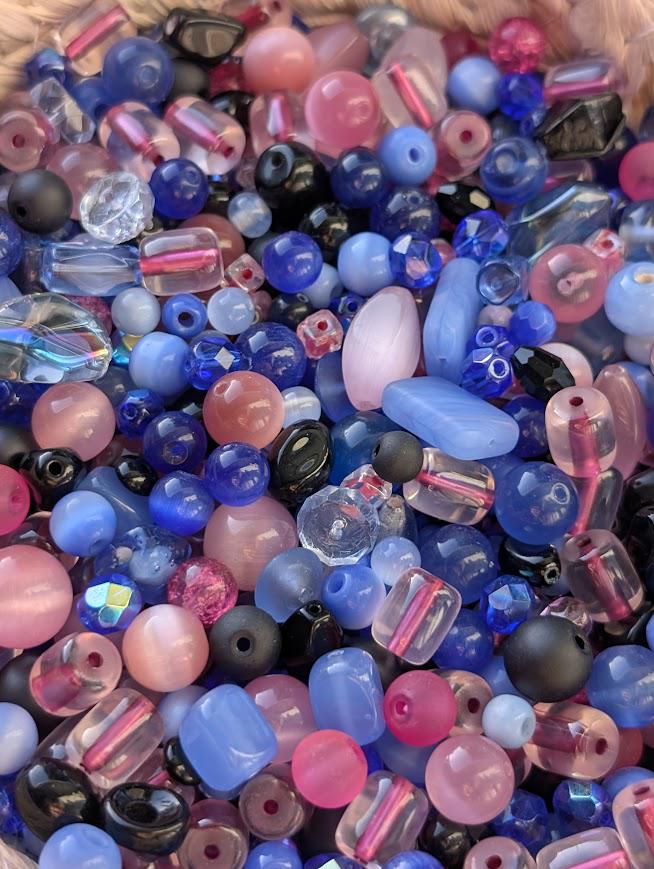 The image is a close-up of a collection of colorful glass beads, including various shades of blue, pink, and purple.