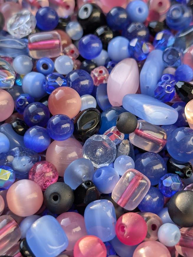 The image is a close-up of a collection of colorful glass beads, including various shades of blue, pink, and black.