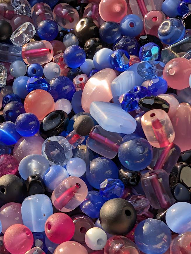 The image is a close-up of a collection of colorful glass beads, including various shades of blue, pink, and black, scattered together.
