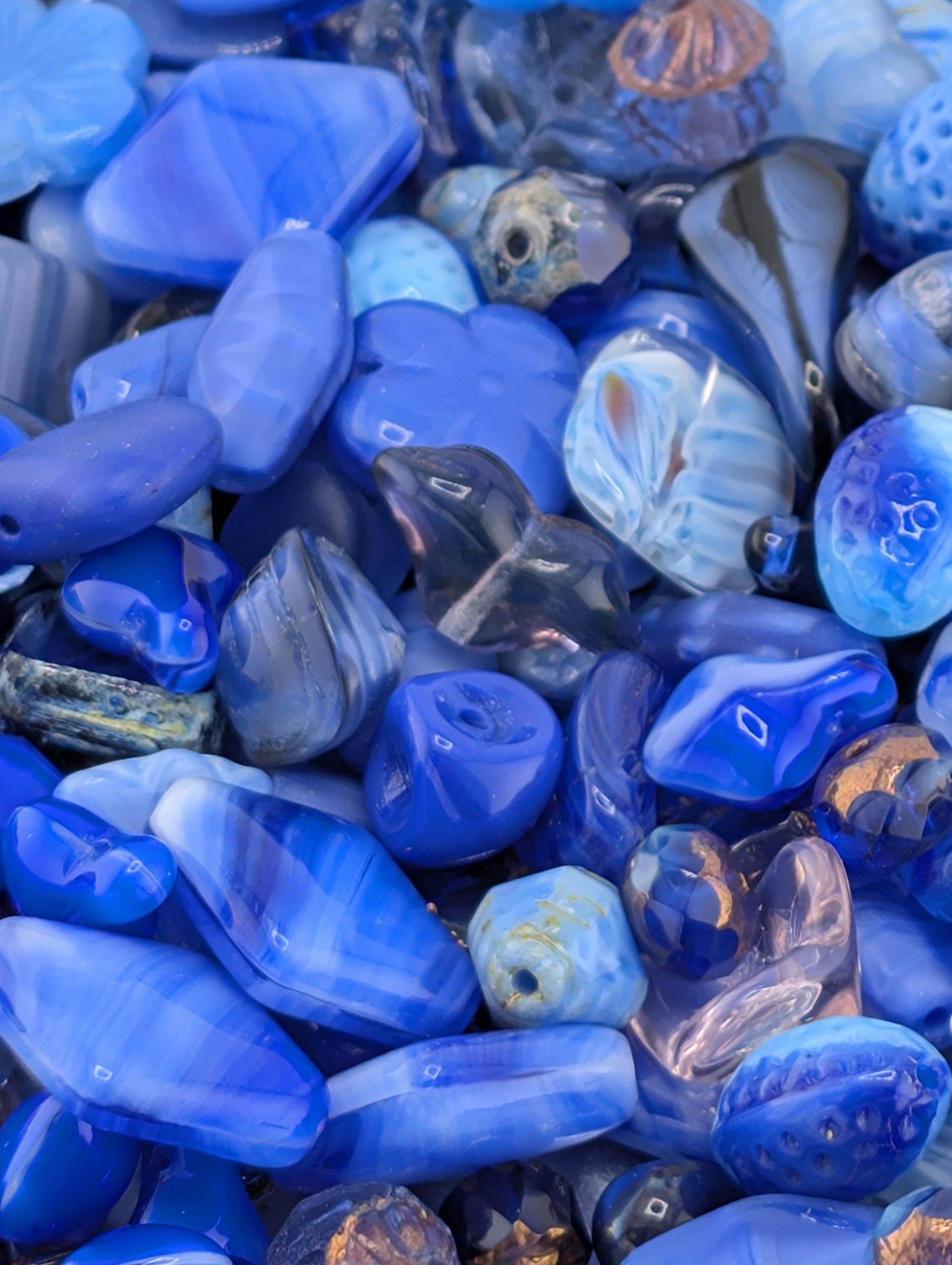 The image is a close-up of various blue and purple glass beads, showcasing their intricate patterns and textures.