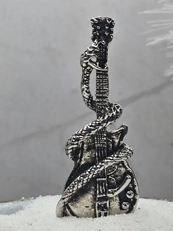 A silver-colored metal sculpture of a guitar with a snake-like design wrapped around it, standing on a snowy surface.