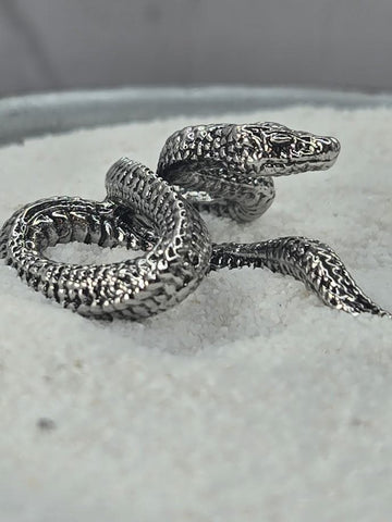 A close-up image of a silver snake-shaped ring resting on a white surface.