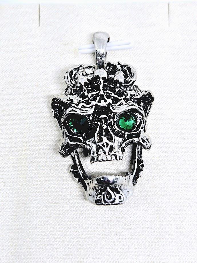 A silver-toned pendant in the shape of a skull with green gemstones on the eyes.