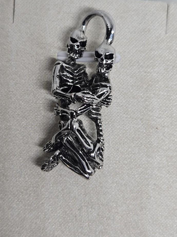 A silver-colored metal sculpture depicting two skeletal figures embracing each other.