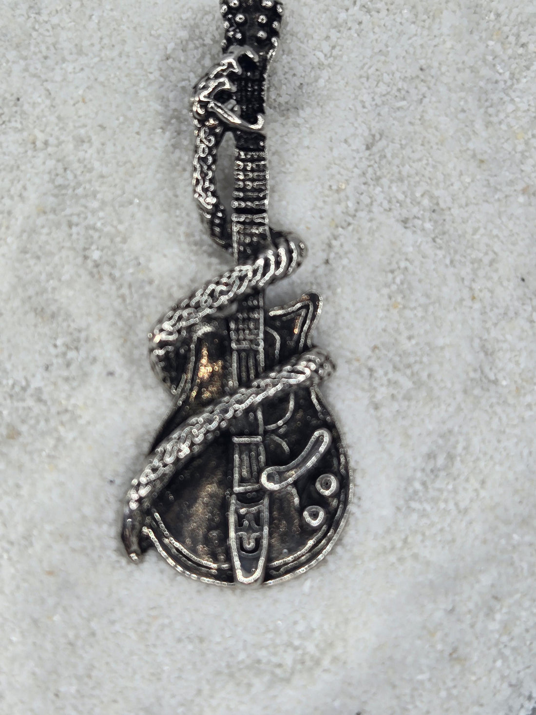 A silver-colored metal sculpture of a guitar with a snake-like design wrapped around it, standing on a snowy surface.
