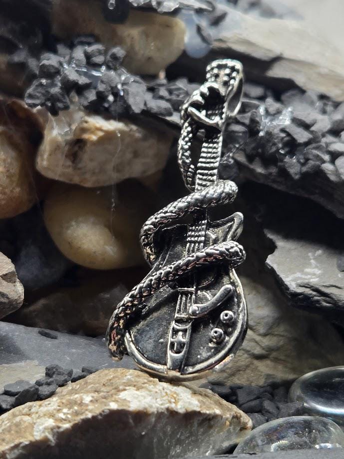 A silver-colored pendant in the shape of a guitar with a snake wrapped around it, resting on a bed of rocks.