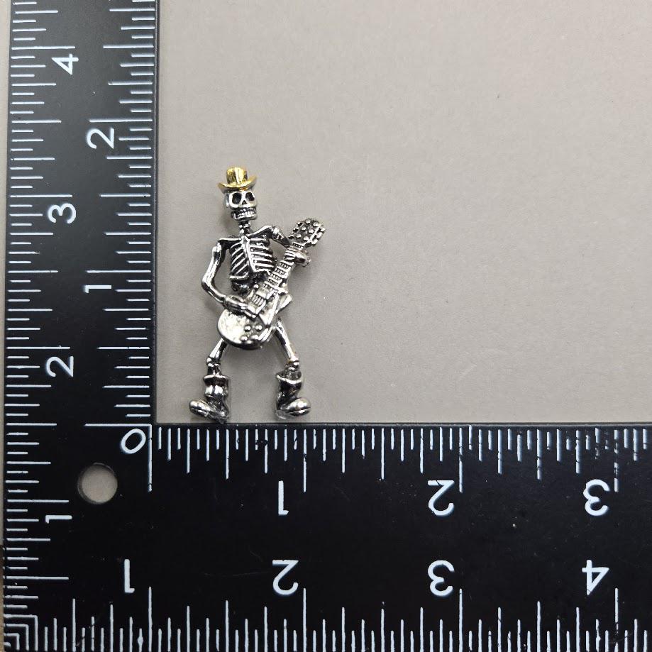 A small silver skeleton figurine is being measured against a ruler.