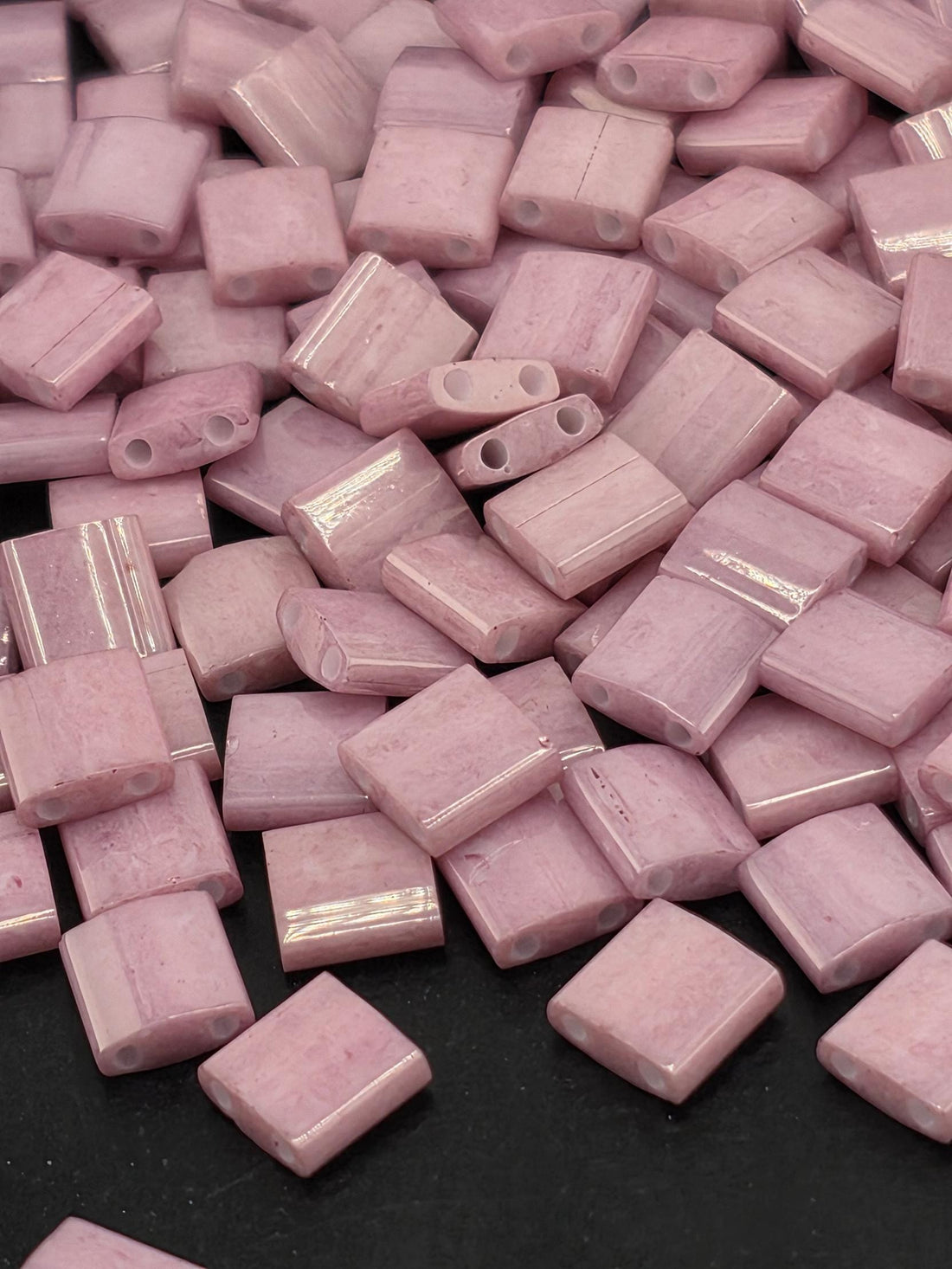 a close-up view of numerous small, square-shaped pink beads scattered on a dark surface.