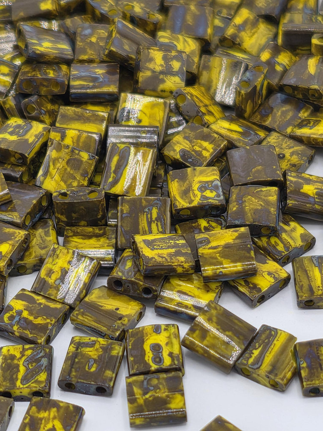 a close-up view of numerous small, square-shaped objects with a yellow and brown color pattern. The objects appear to be made of a material that resembles wood or metal, and they are scattered across a surface.