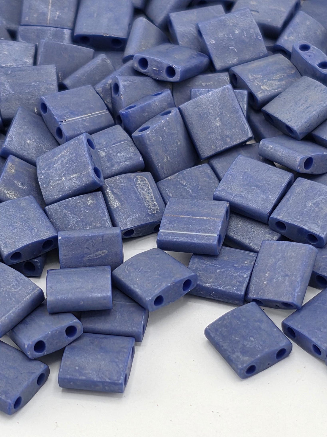 A pile of small, square-shaped blue beads or objects with a textured surface.