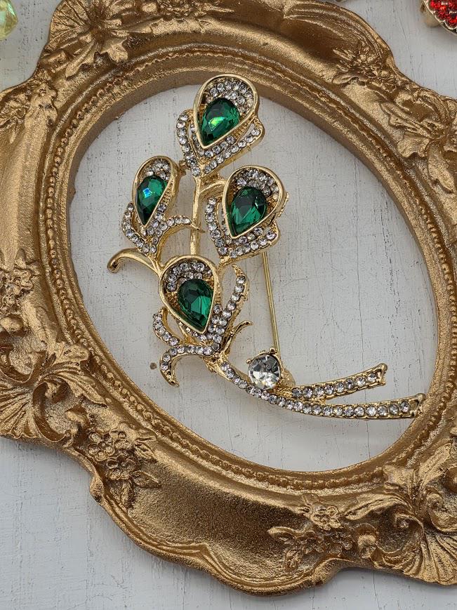 a decorative gold-colored frame with a brooch adorned with green gemstones.