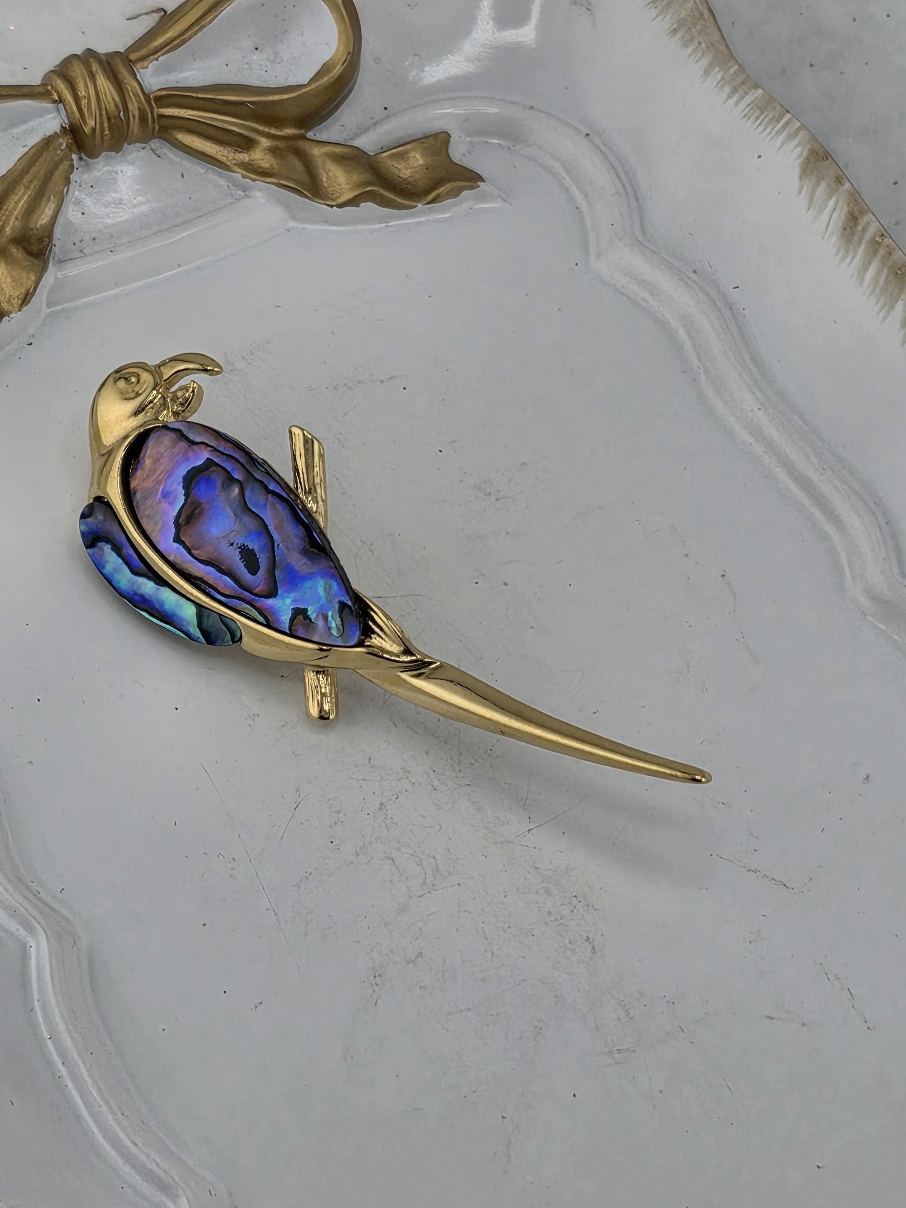 A gold-colored bird-shaped brooch with a colorful iridescent stone in the shape of a bird's head and beak.