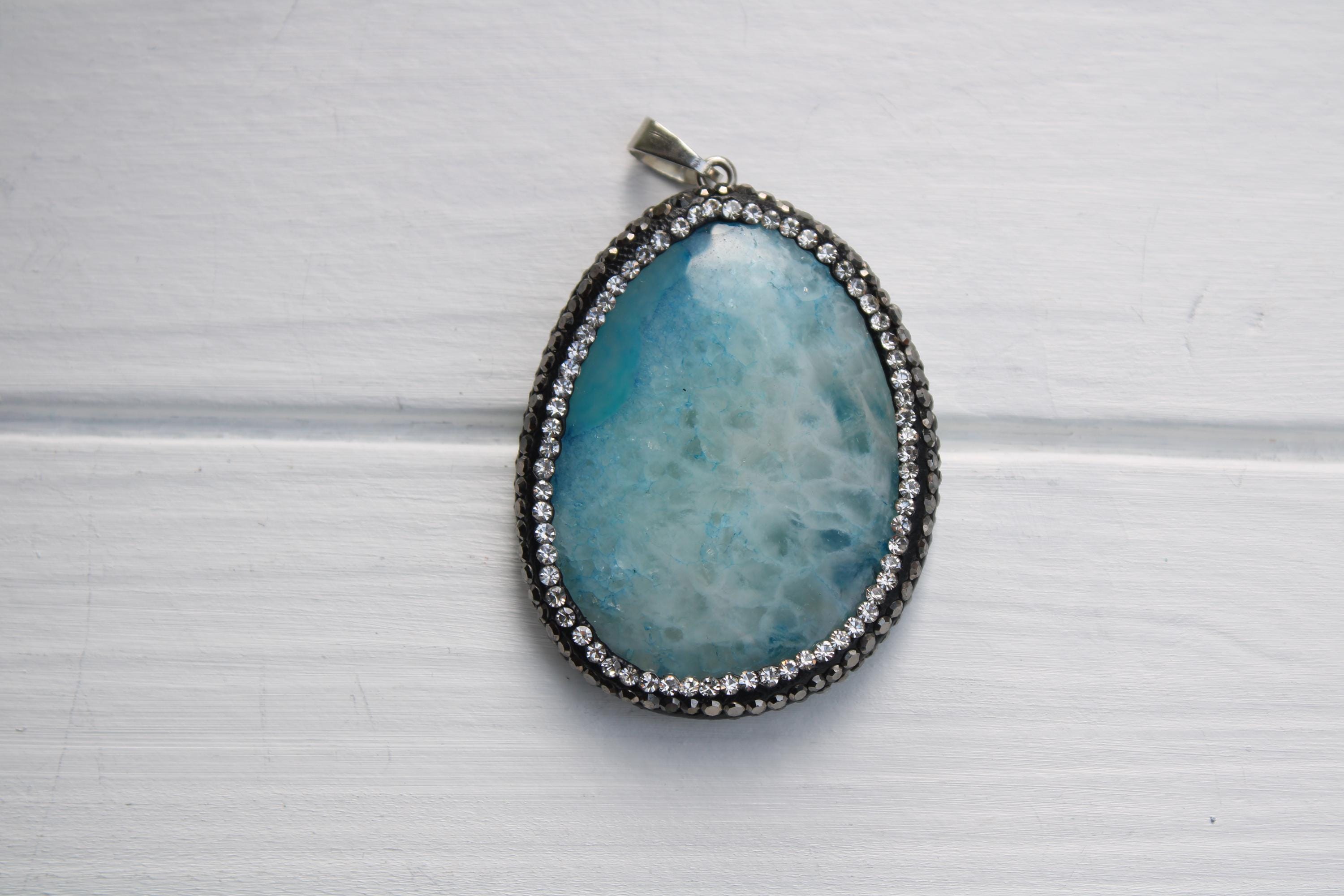 A pendant with a blue stone and a silver frame, set against a white background.