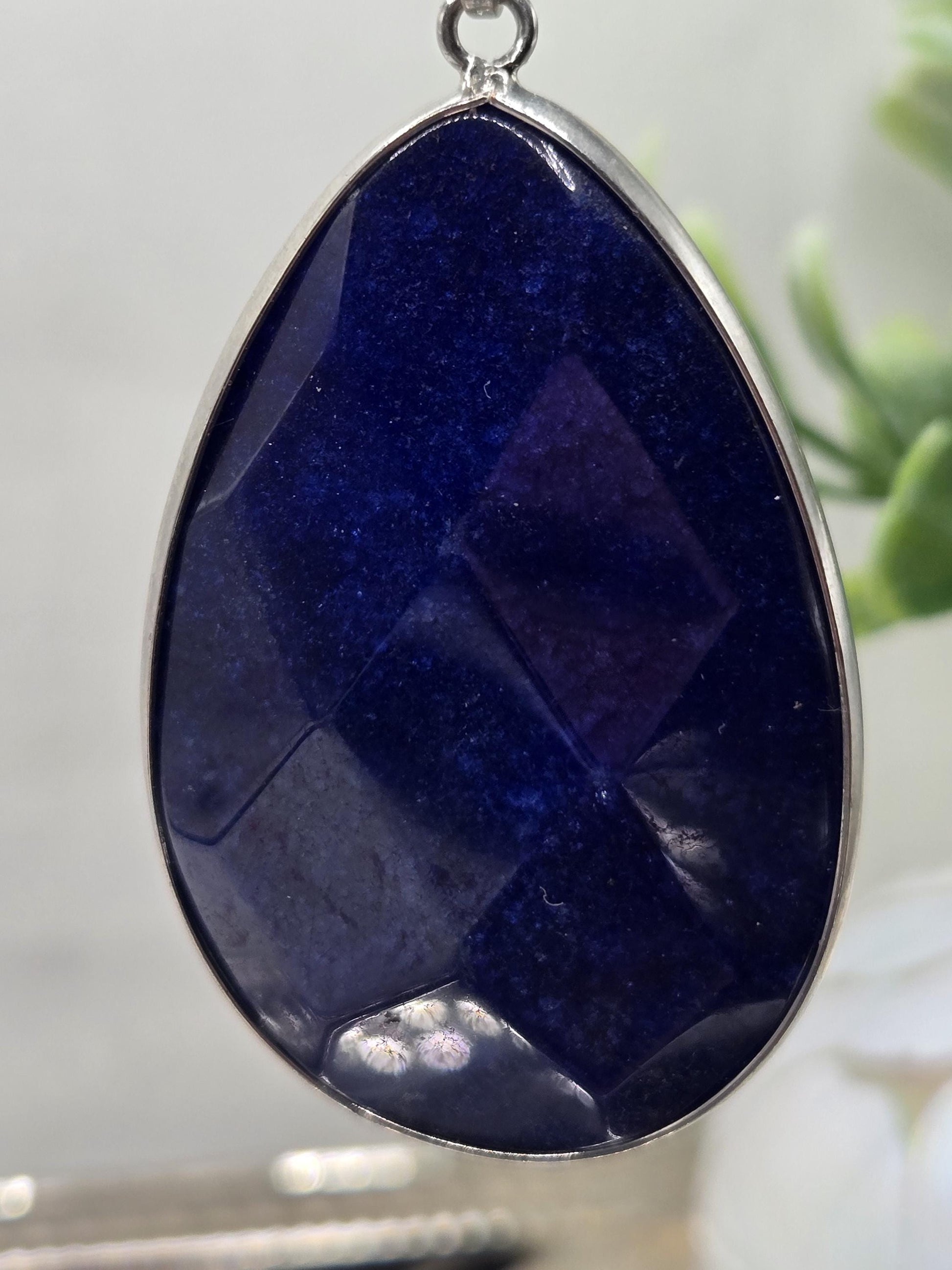 A close-up image of a large, oval-shaped blue gemstone with a metallic frame, set against a blurred background.
