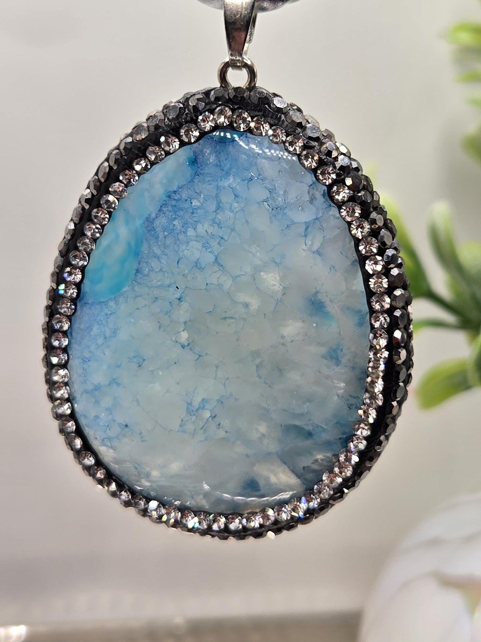 A close-up image of a pendant featuring a large, blue-green stone with a sparkling crystal frame.