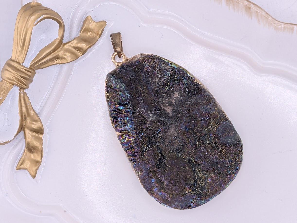 A large, irregularly shaped, multicolored rock with a rough, jagged surface is displayed on a white surface, accompanied by a gold ribbon.