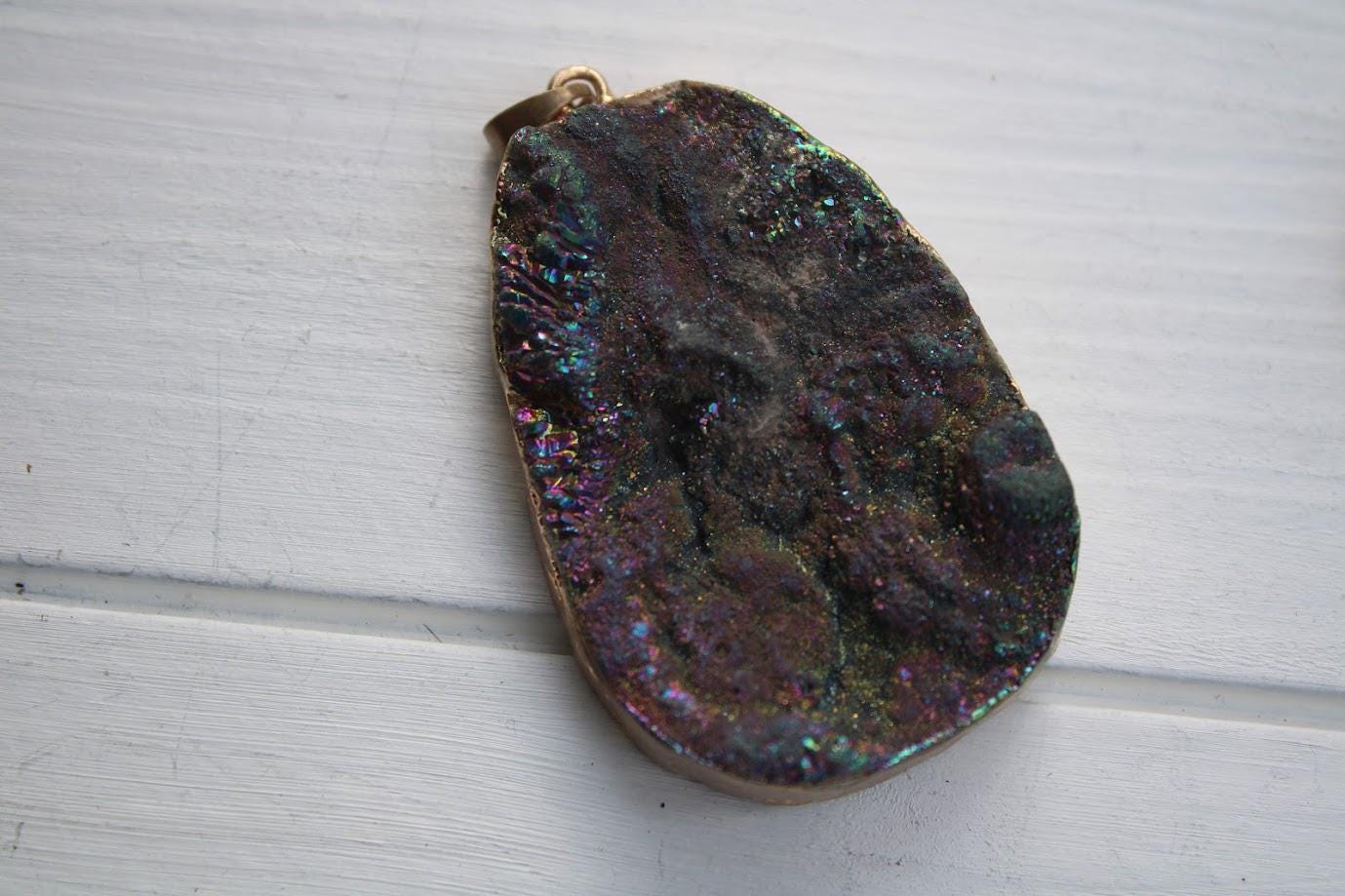 A close-up image of a colorful, irregularly shaped rock or gemstone with a metallic sheen, resting on a white surface.