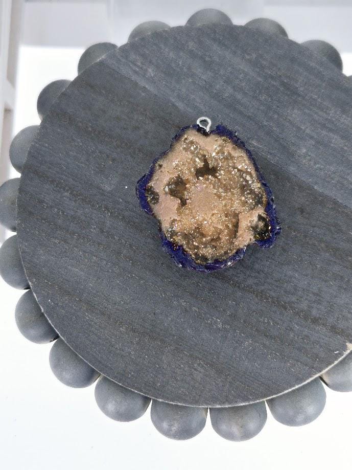 a piece of geode, a natural rock formation, with a blue and purple border, resting on a gray circular surface.