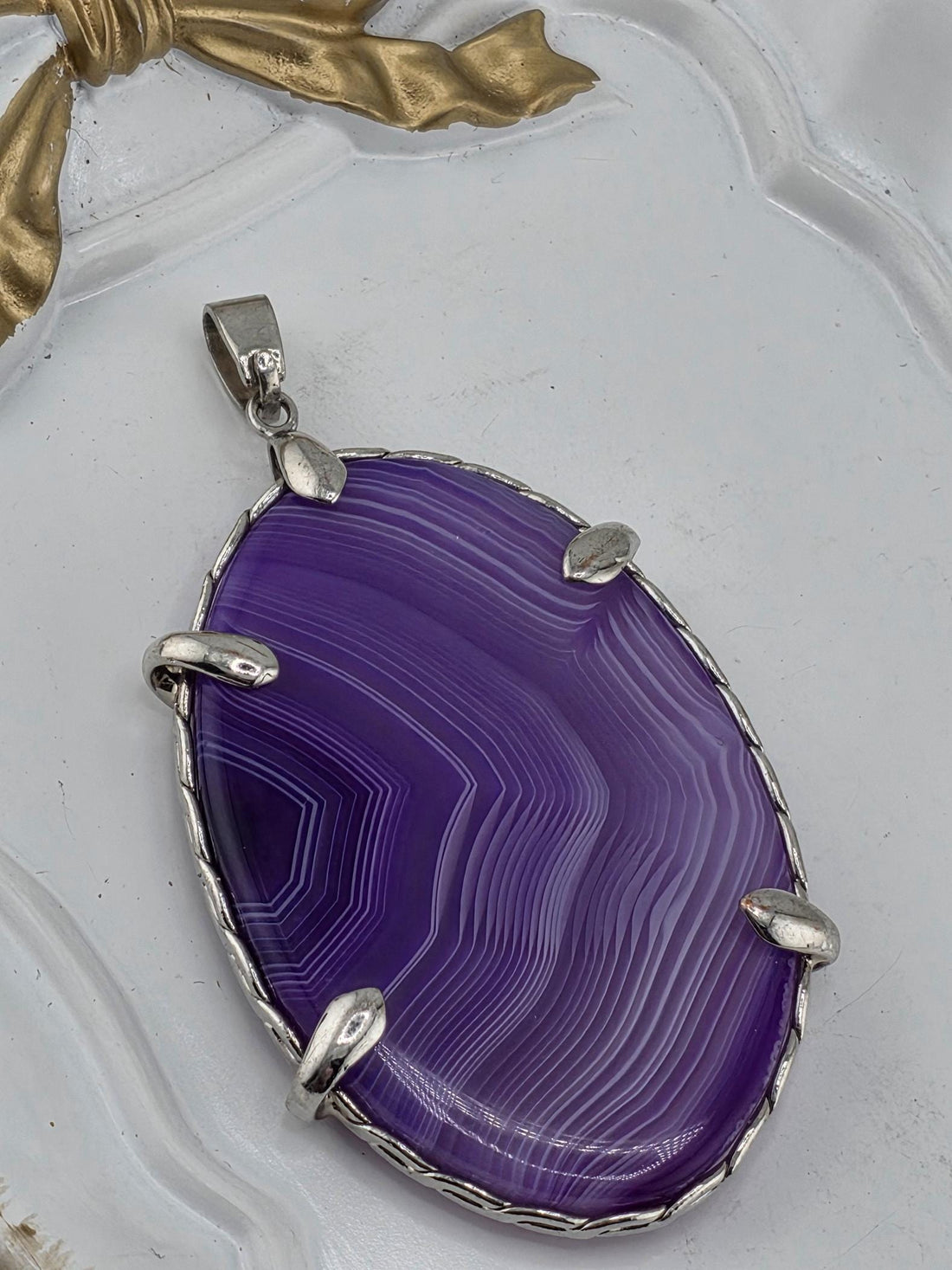 A purple agate stone with a silver pendant is displayed on a white surface.