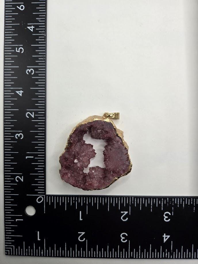 A pendant made of a purple gemstone is displayed on a white surface, accompanied by a gold ribbon.