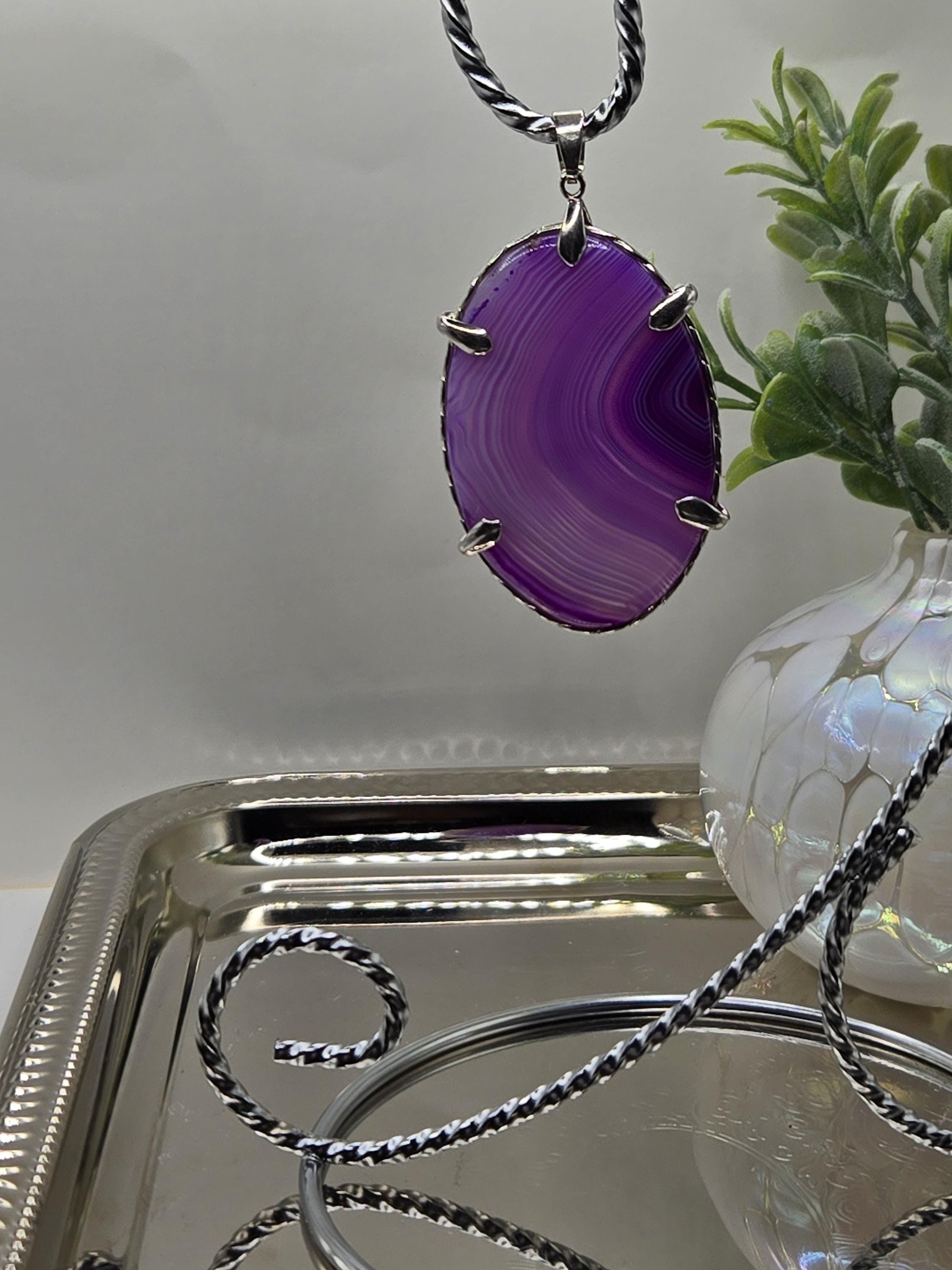 a purple stone pendant with a silver chain, hanging from a silver tray.