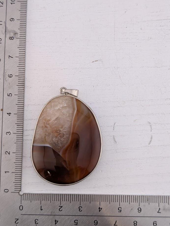 a pendant with a large, oval-shaped stone in the center, resting on a ruler for size comparison.