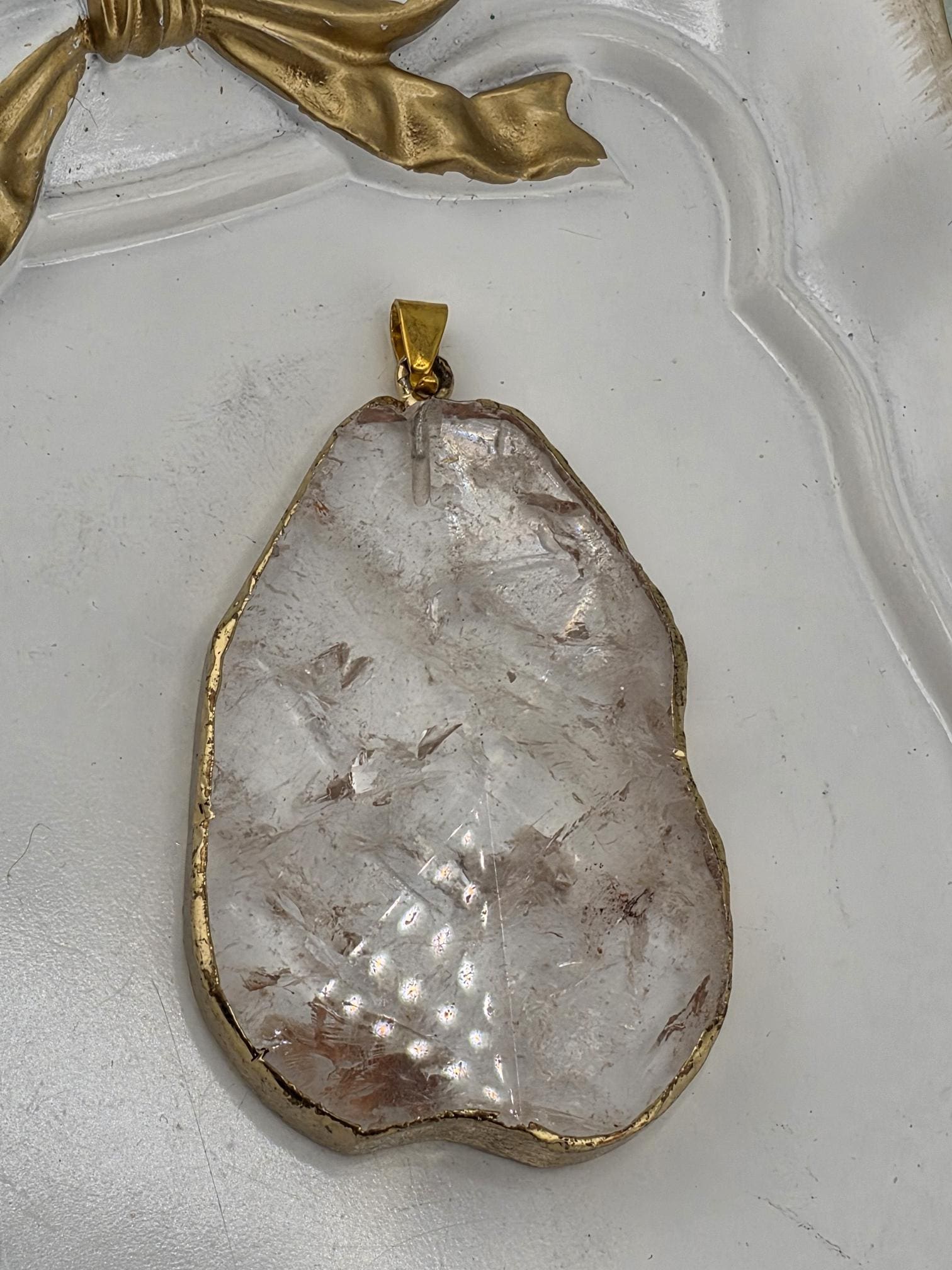 A large, clear crystal pendant with a gold-colored frame is displayed on a white surface.