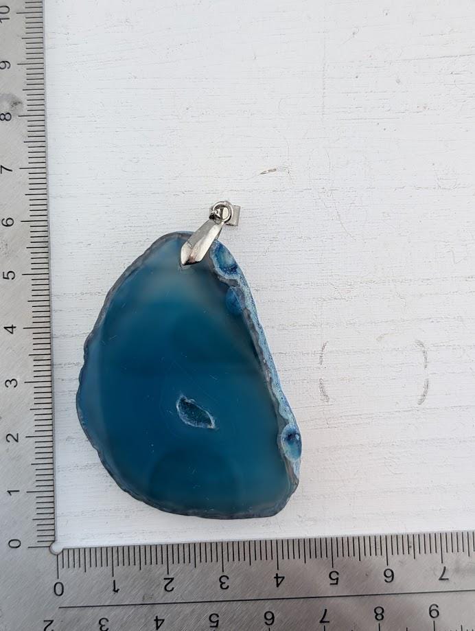 A blue agate stone with a small hole in the center, placed on a white surface.