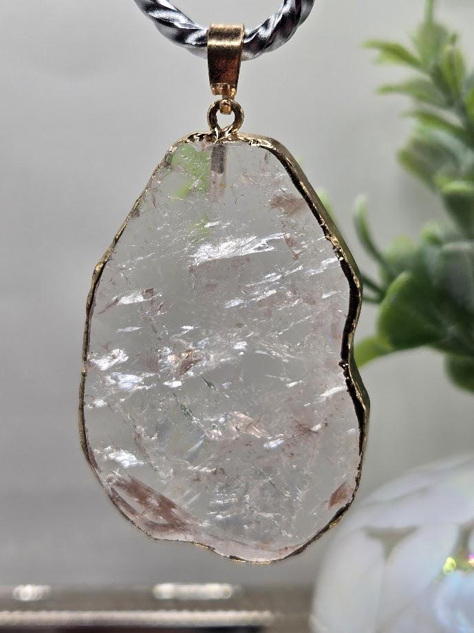 A large, clear crystal pendant with a gold-colored frame hangs from a silver chain.